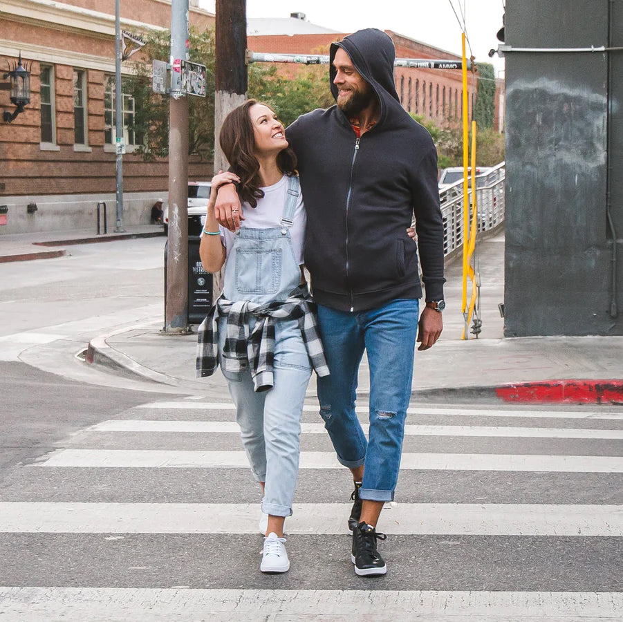 A couple walking in a cross walk looking at each other wearing white and black leather sneakers