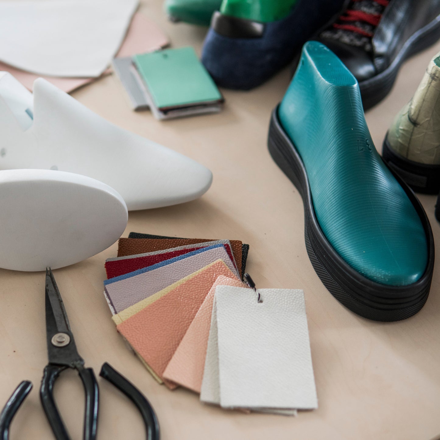 Picture of shoe lasts with some swatches of leather options that could be used for a custom shoe and a shoe last sitting on a black cupsole