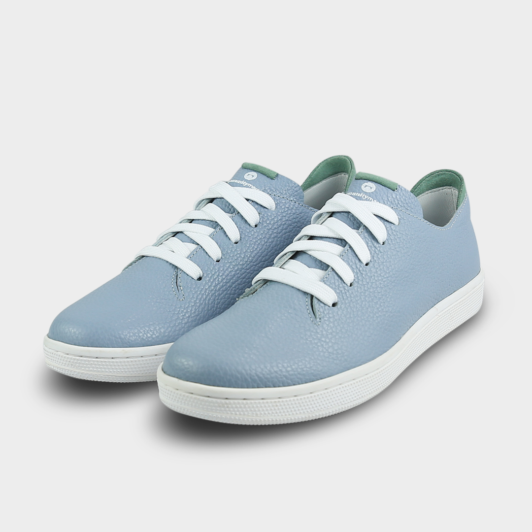 A quarter angle shot of pair of sky blue leather sneakers with a lace-up closure featuring flat white shoelaces, a white rubber cupsole and a green accent on the heel.