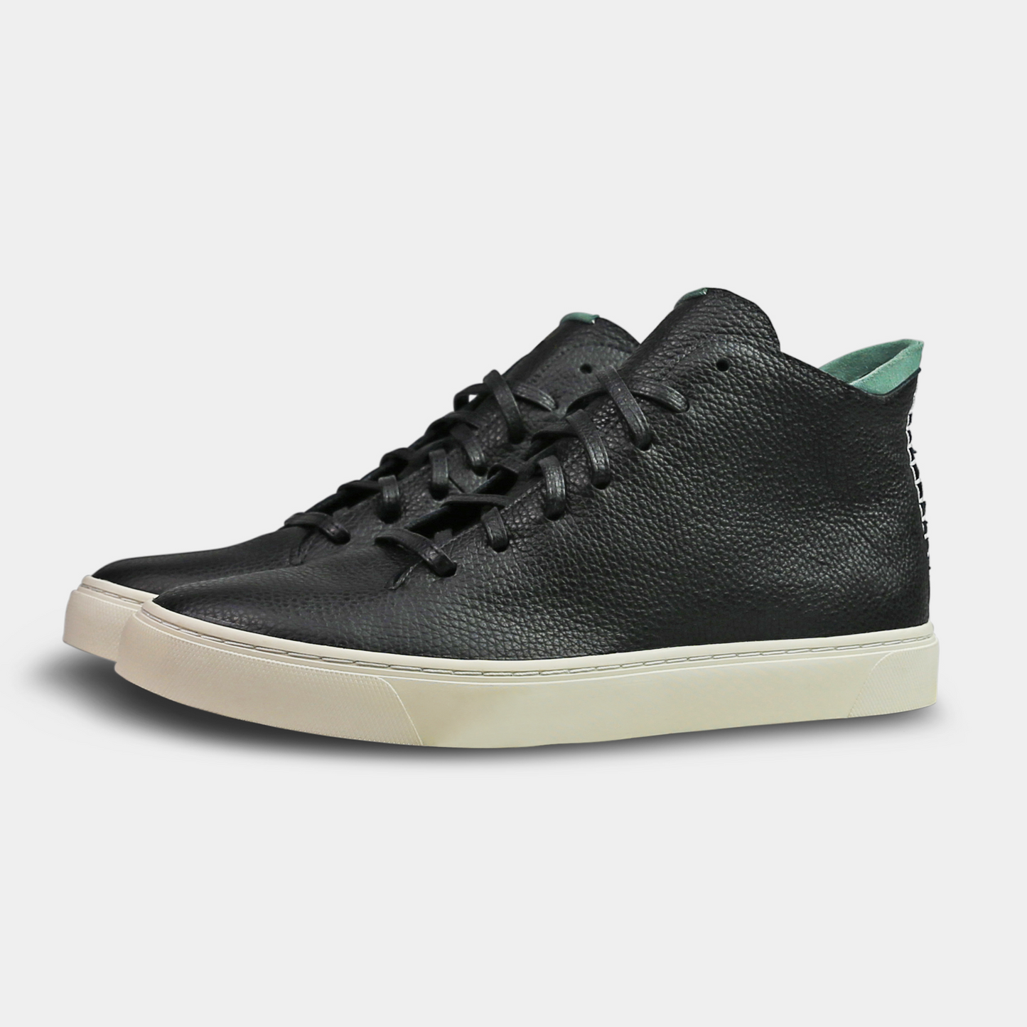 A black, mid-top sneaker with a leather upper, lace-up closure, and a white sole quarter view